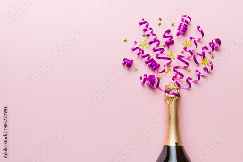 Creative flat lay composition with bottle of champagne and space for text on color background. Champagne bottle with colorful party streamers. holiday or christmas concept