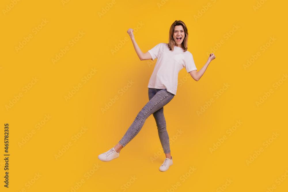 Photo of excited funny carefree lady dance have fun wear casual t-shirt jeans sneakers on yellow background