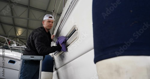 Young handsome professional guy (male) cleaner, washes the yacht after polishing and lining ceramics on the yacht. Concept of: Ceramics, Cleaning, New Ship, Polishing, Cleaner, In Robe, Cap, Hard Work