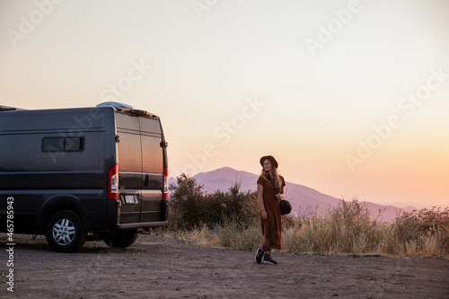 hipster girl living in van wearing hat overlooking sunset in the mountains
