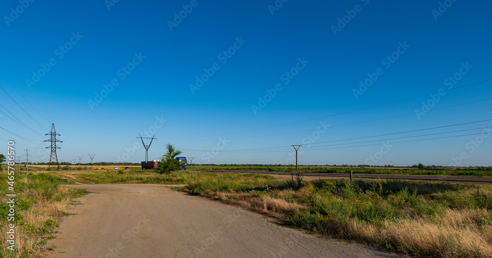The road in the green field and high-voltage poles. Landscape and electricity