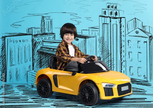 Cute little boy driving toy car and drawing of city on light blue background photo