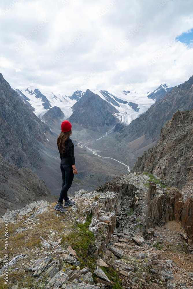 Sports girl in a red hat stands on the top of the mountain