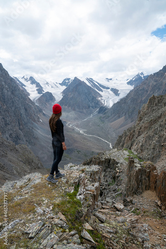Sports girl in a red hat stands on the top of the mountain