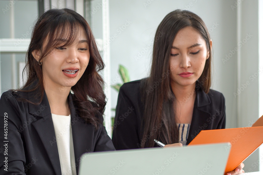 An Asian businesswoman uses a laptop to search and explain information to her secretary to write down notes in a folder. An Asian businesswoman uses a laptop to search and explain information to her secretary to write down notes in a folder.
