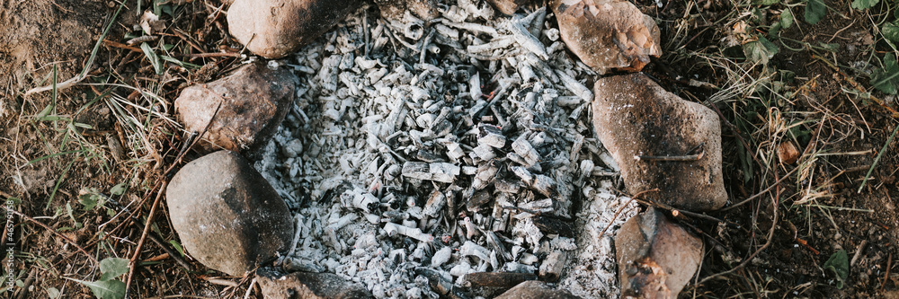 smoldering and ember gray coals and ashes from an extinct campfire in small children's bonfire made of stones on the ground on summer or autumn evening. countryside and rustic scene. top view. banner smoldering and ember gray coals and ashes from an extinct campfire in small children's bonfire made of stones on the ground on summer or autumn evening. countryside and rustic scene. top view. banner
