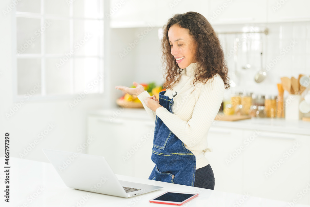 Portrait of beautiful young black woman is live streaming cooking with laptop in the bright white kitchen. wife or housewife is preparing to cook healthy food for the family. Stay at home. Portrait of beautiful young black woman is live streaming cooking with laptop in the bright white kitchen. wife or housewife is preparing to cook healthy food for the family. Stay at home.