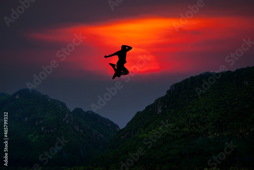  Silhouette of man jumping over mountain On the background of the evening sun