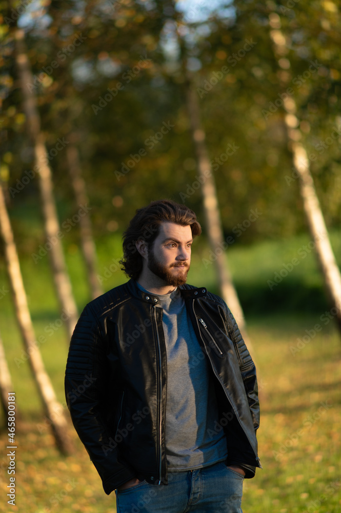 Young bearded man standing and looking at distance against a background of colorful autumn trees Young bearded man standing and looking at distance against a background of colorful autumn trees