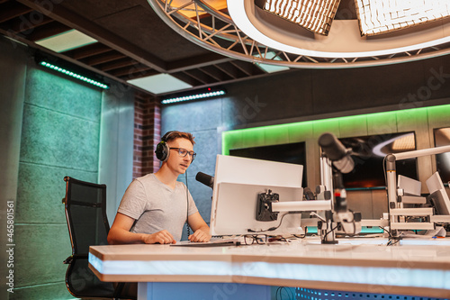 The DJ hosts the program and communicates with the audience on air at the radio station. The announcer reads the news. A male radio host speaks into a microphone and records a podcast photo