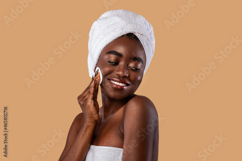 Portrait of happy black woman cleaning skin by cotton pad