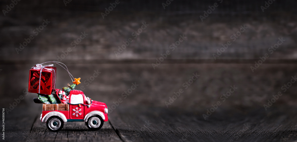 Toy of car with New year fir tree and red gift box on wooden rustic background. Long banner