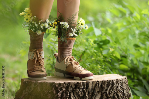 Woman standing on stump with flowers in socks outdoors, closeup photo