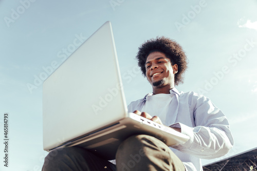 Obraz na plátně close up from below of young african student working in laptop outdoors