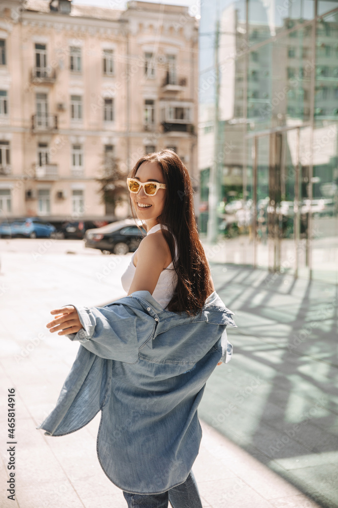 Full-length image of feminine asian on blurred background of city. Long-haired brunette in blouse and shirt top, sunglasses on her face. Good mood, fashion trends Full-length image of feminine asian on blurred background of city. Long-haired brunette in blouse and shirt top, sunglasses on her face. Good mood, fashion trends