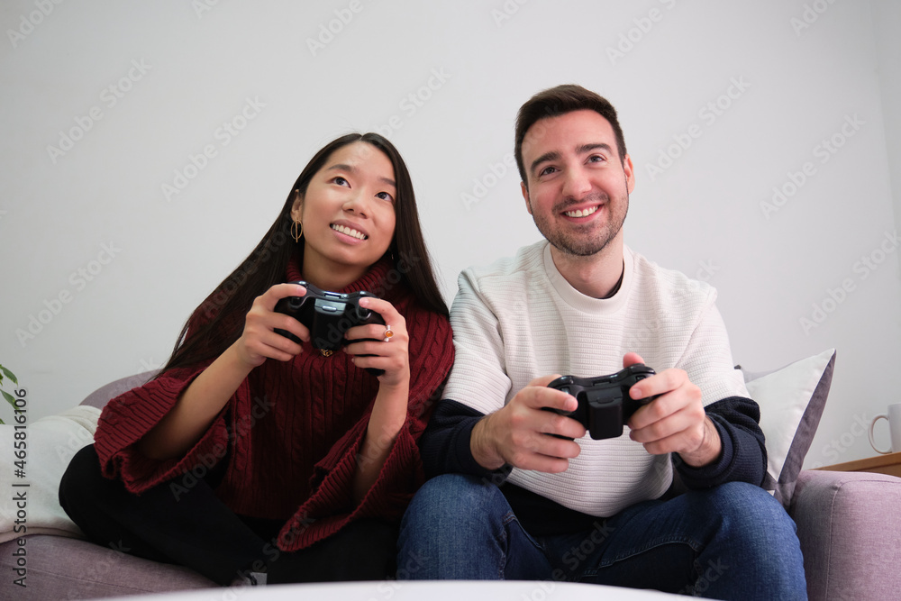 Fototapeta premium Young multiracial couple playing video games and using joystick controllers.