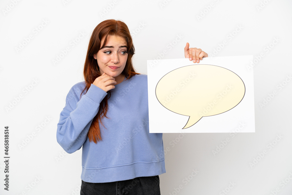 Young redhead woman isolated on white background holding a placard with speech bubble icon and thinking Young redhead woman isolated on white background holding a placard with speech bubble icon and thinking