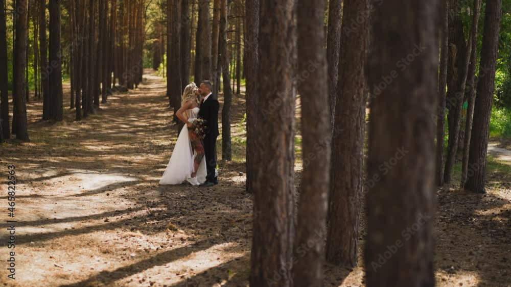 Seductive woman young wife in frank wedding dress with tattoos on bare leg kisses beloved husband standing in green city park slow motion Seductive woman young wife in frank wedding dress with tattoos on bare leg kisses beloved husband standing in green city park slow motion