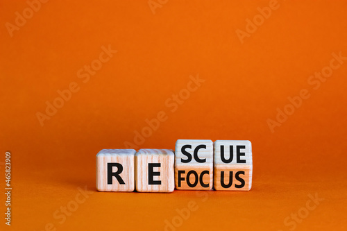 Refocus and rescue symbol. Businessman turned cubes and changed the word 'refocus' to 'rescue'. Beautiful orange table, orange background. Business refocus and rescue concept. Copy space.