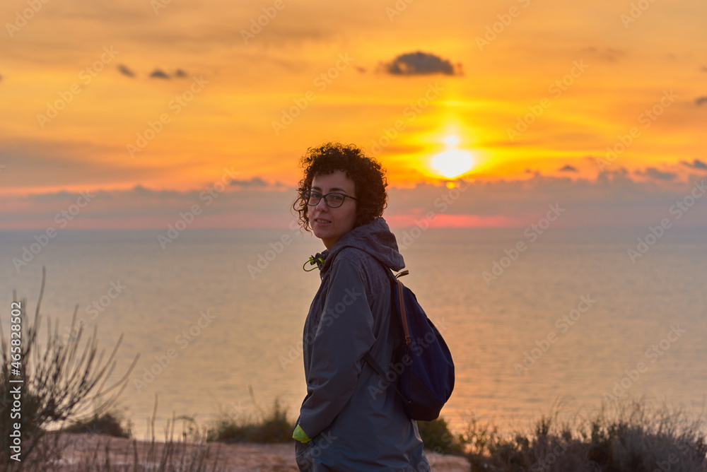Fototapeta premium Hiker woman looking at camera while sunrise at sea