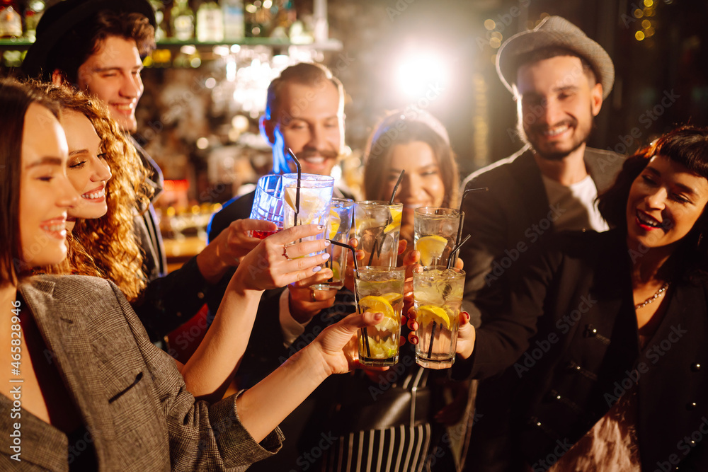 Cheering and drinking cocktails. Group of friends partying in a nightclub and toasting drinks with cocktails. Happy people enjoying winter holiday. Party, celebration, drink, birthday concept.