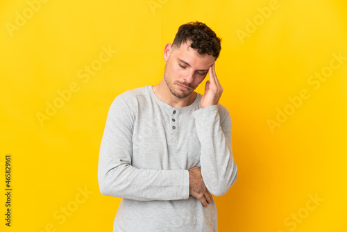 Young caucasian handsome man isolated on yellow background with headache
