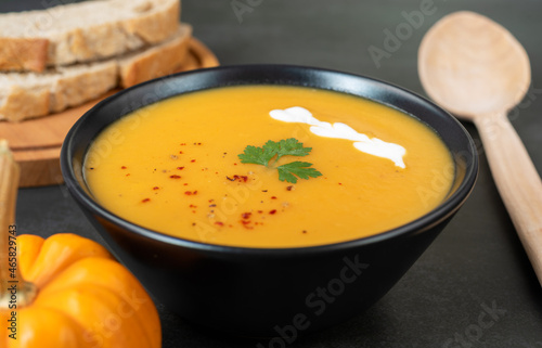 Warming pumpkin cream soup on a black background with a wooden spoon.