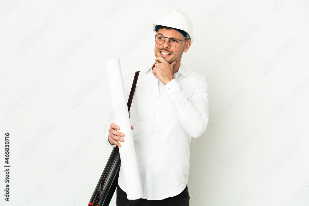 Young architect man with helmet and holding blueprints isolated on white background looking to the side and smiling Young architect man with helmet and holding blueprints isolated on white background looking to the side and smiling