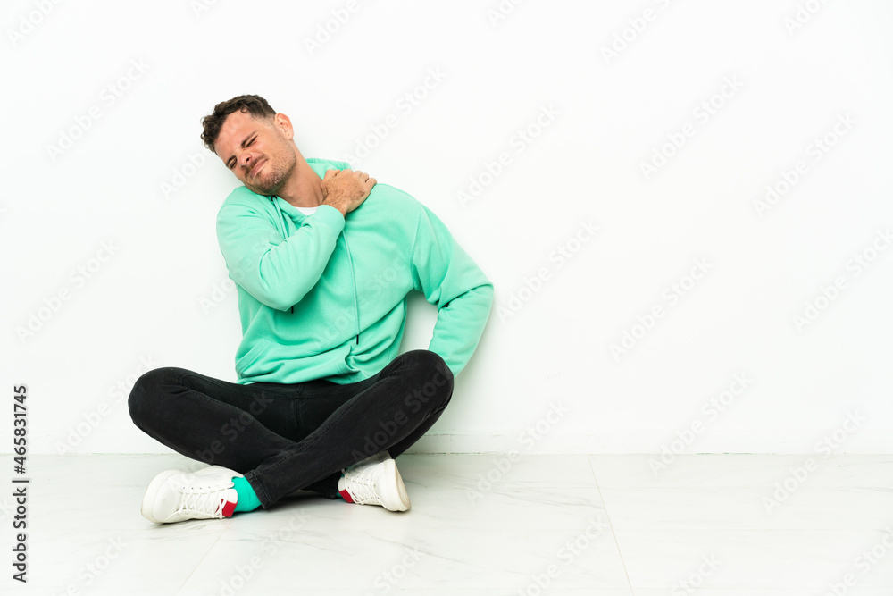 Young handsome caucasian man sitting on the floor suffering from pain in shoulder for having made an effort