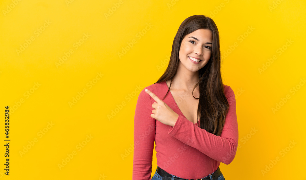 Obraz premium Teenager Brazilian girl over isolated yellow background pointing to the side to present a product