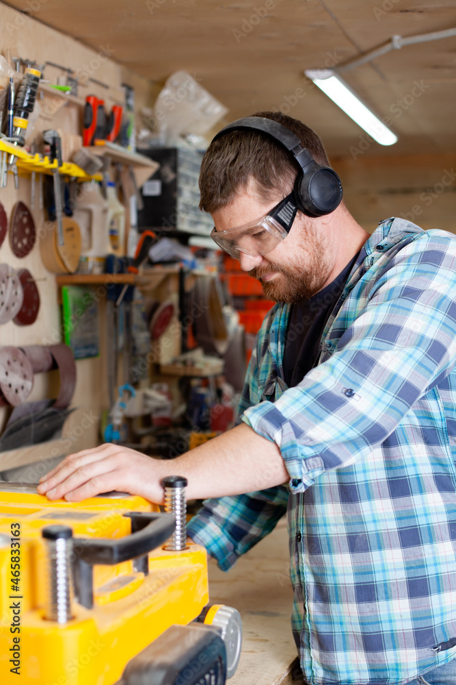 A carpenter in a plaid shirt works at a machine in a workshop. Wood. Ecological compatibility. Lifestyle. A carpenter in a plaid shirt works at a machine in a workshop. Wood. Ecological compatibility. Lifestyle.