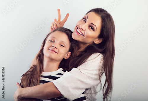 Happy laughing beautiful mother hugging her smiling daughter with love and showing the fun horns by fingers on studio background photo
