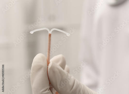 Doctor holding T-shaped intrauterine birth control device on blurred background  closeup