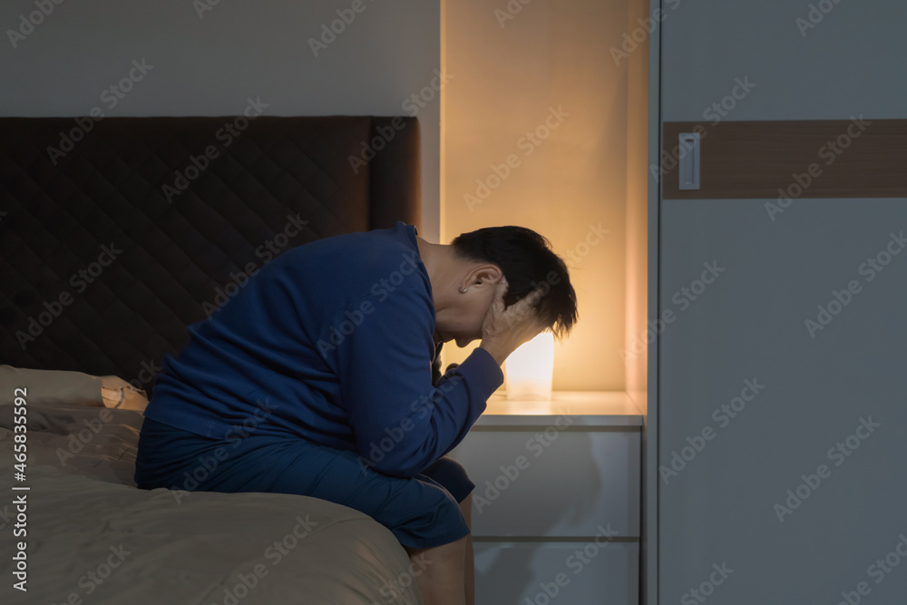Depressed lonely elderly old Asian woman, people sitting on bed in bedroom at home. Lifestyle on late night. Insomnia. Quarantine