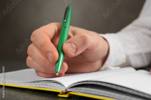 Man writing with pen in notebook at grey table, closeup of hand