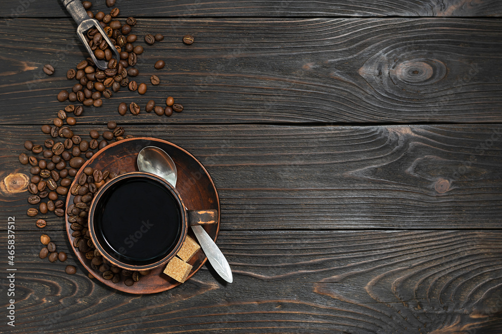 Fototapeta Black coffee in a clay cup on dark wooden boards. Coffee beans are scattered in the background. Top view, space for text