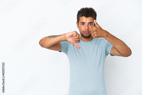Young handsome Brazilian man isolated on white background making good-bad sign. Undecided between yes or not