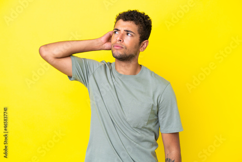 Young handsome Brazilian man isolated on yellow background having doubts