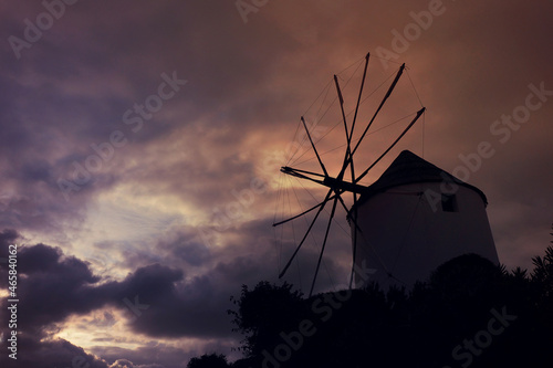 Dramatic mood of traditional windmill as seen with colourful sunset and clouds in Cycladic destination island