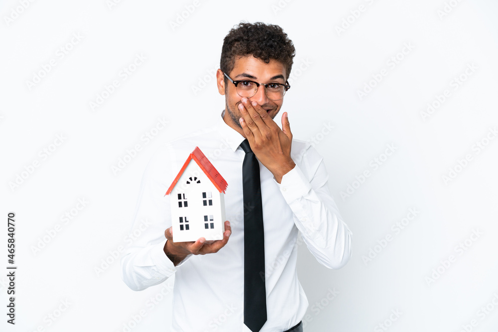 Young business Brazilian man holding a house toy isolated on white background happy and smiling covering mouth with hand Young business Brazilian man holding a house toy isolated on white background happy and smiling covering mouth with hand