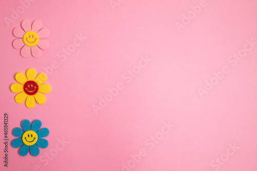 Three colorful flowers on left side with smile face. Pink background.