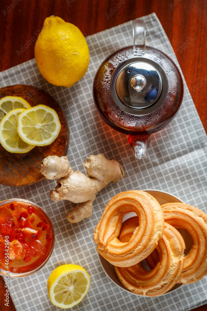 A kettle of strong infused tea on a napkin next to lemon, ginger and jam and donuts. A kettle of strong infused tea on a napkin next to lemon, ginger and jam and donuts.