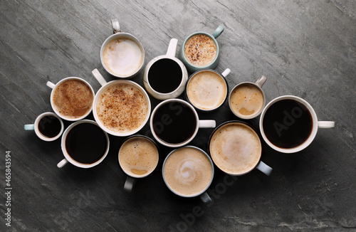 Many cups of different coffees on slate table, flat lay