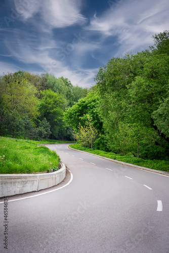 asphalt road through the green field and clouds on blue sky