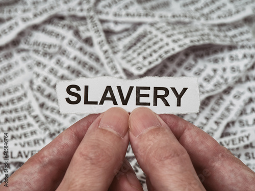 A man holding a torn piece of paper with the word Slavery on it in his hands above a pile of pieces of paper that have the word slavery on them
