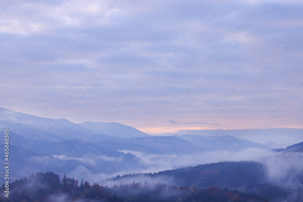 Beautiful view of mountains covered with fog and cloudy sky during sunrise