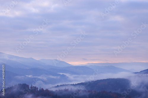 Beautiful view of mountains covered with fog and cloudy sky during sunrise
