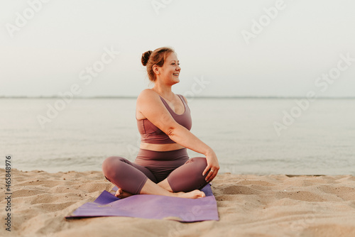 Caucasian woman practicing yoga at seashore sandy beach on sunrise. Womens health and wellness. Sports body positive