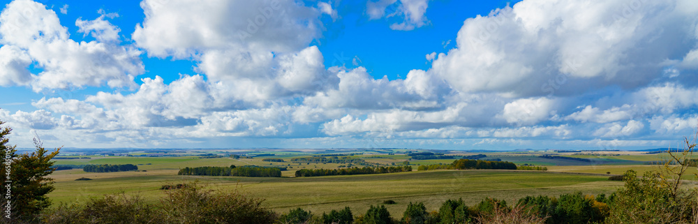 a panoramic long English countryside view of green fields, woodlands and a big blue and white cloud sky, viewed Westerly from Sidbury Hill, Wiltshire UK