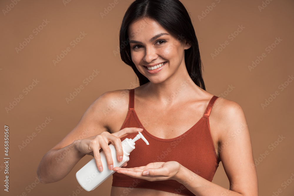 Caucasian brunette lady with cheerful smile hold cosmetic bottle in studio